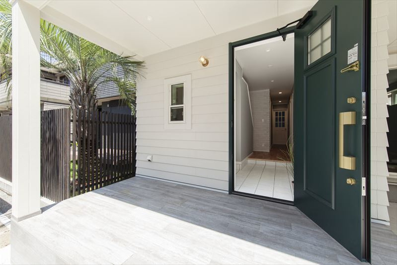 白のサイディングと重厚な玄関ドアの広い玄関ポーチ